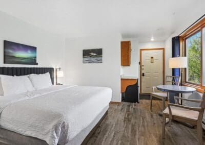 King bed below a northern lights print, with the entry door and window seating beyond