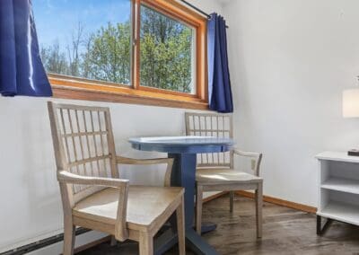 A table and two wooden chairs by the window of a King Room, looking out to trees