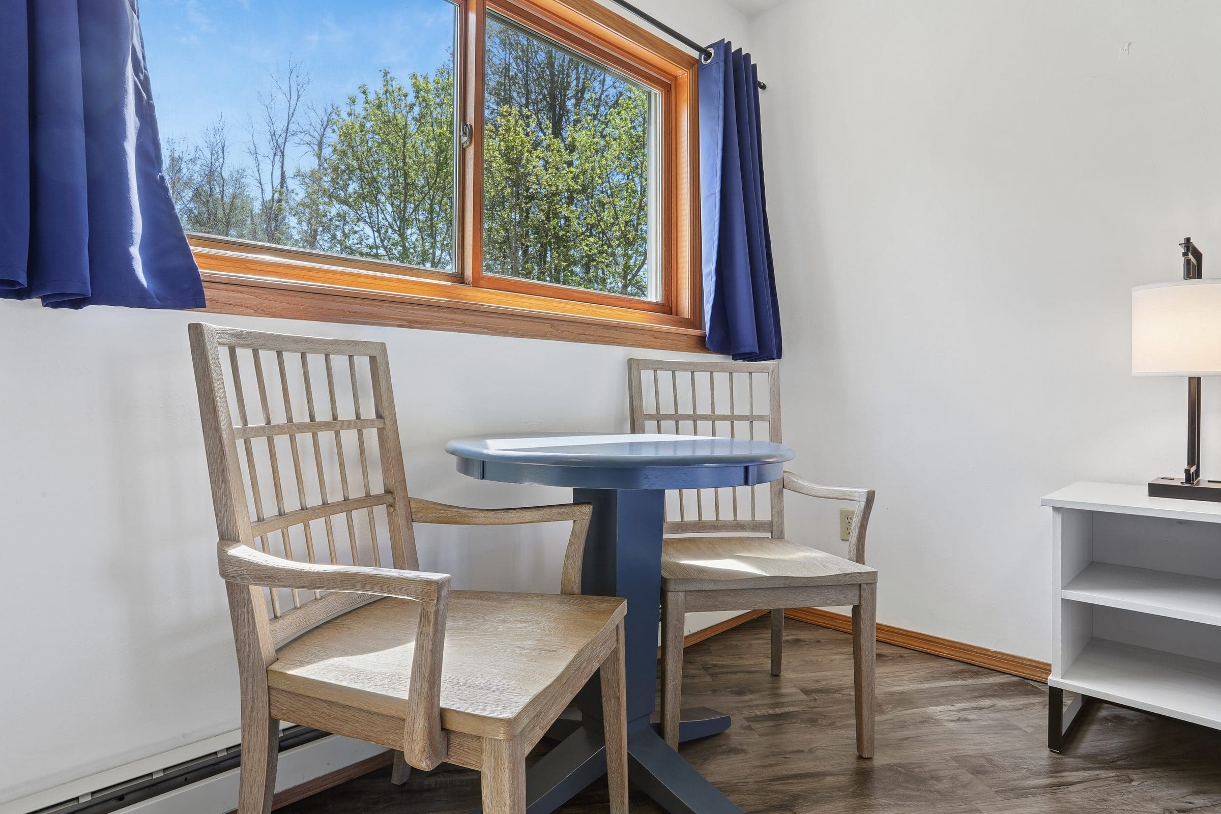 A table and two wooden chairs by the window of a King Room, looking out to trees