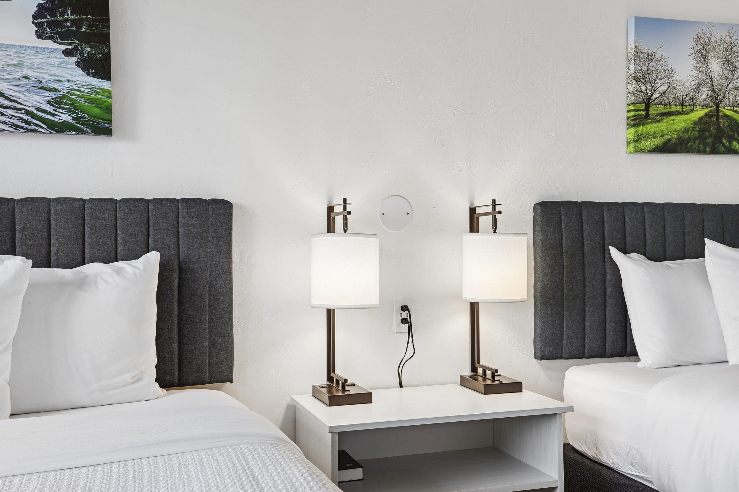 Charcoal upholstered headboards and a shared nightstand between the two queen beds