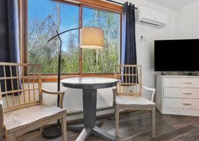 Two chairs and a small table by the window in a Two Queen Room, with trees outside