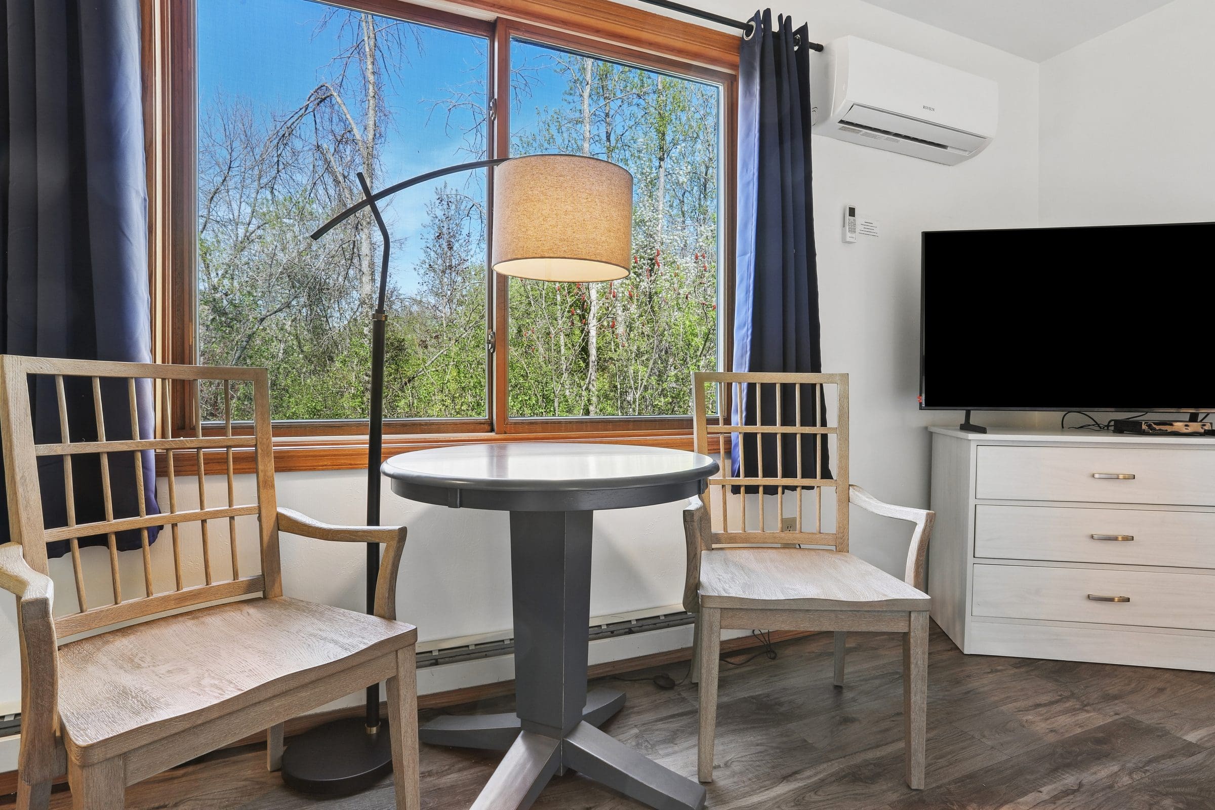 Two chairs and a small table by the window in a Two Queen Room, with trees outside